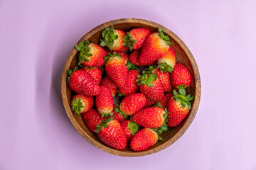 Fresh red strawberries in wooden bowl top view. Strawberry fruits on purple background. Organic food theme.
