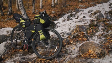 The mixed terrain cycle touring bike with bikepacking. The travel journey with light bicycle bags designed or modified for cycling. The trip on bike, outdoor in magical autumn forest, river stream.