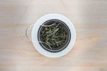 Bai Mu Dan (White peony) fresh white tea leaves. From Fujian province, China. Close up of wet leaves in a teapot metal filter on a white porcelain plate and a wooden table. Top view