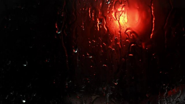 Background with raindrops on a black background for overlay to create mood. Light water on window with red light outside. Wet noir background