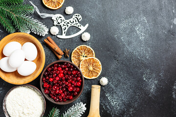 Christmas baking ingredients on black rustic background with festive decorations and copy space for your design.