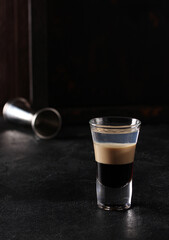 Alcoholic beverage. The b-52. Cocktail of coffee, cream and orange liqueur in a transparent glass on a black background. Bar menu. Background image, copy space, vertical