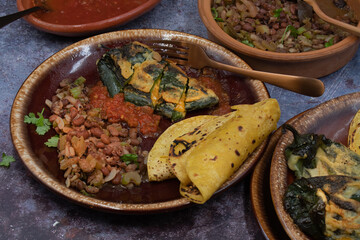 Mexican chiles rellenos with salsa, refried beans and corn tortillas on rustic table