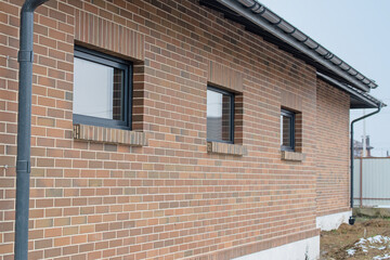 Part of wall made of the brown brick, fragment of roof of modern private dwelling house against of sky