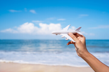 Hand holding a miniature airplane at the tropical beach on a sunny day, Summer vacation and travel concept