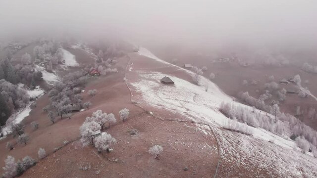 Aerial view of wintertime scene in the Transylvanian village, Pestera, with white frost, fresh snow, blizzard, and fog, at the foot of the Carpathian Mountains