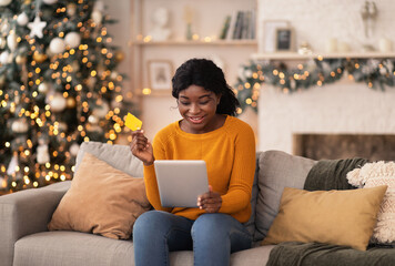 Smiling african american millennial female uses tablet and credit card to shop online in living room