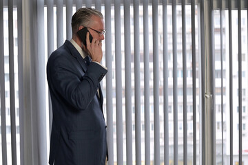 A solid man, director of firm is talking on the phone and looking out the window