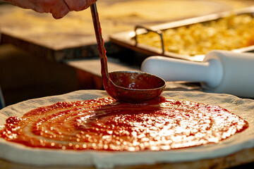 Chef preparing and putting tomato sauce on the pizza dough before entering the wood oven