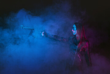 Futuristic girl soldier with a gun in the smoke on the dark background.