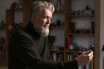 An adult gray-haired man with a beard makes a video call to his relatives, side view