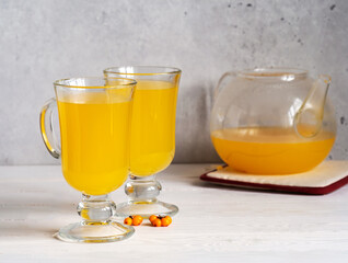 Beautiful tasty and healthy sea buckthorn drink in a glass teapot and in two glasses on a light gray background