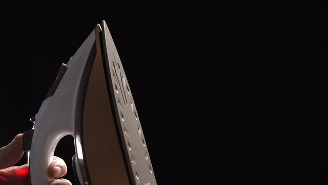 The iron is releasing steam on a black background. Close-up. Household electrical appliances concept.