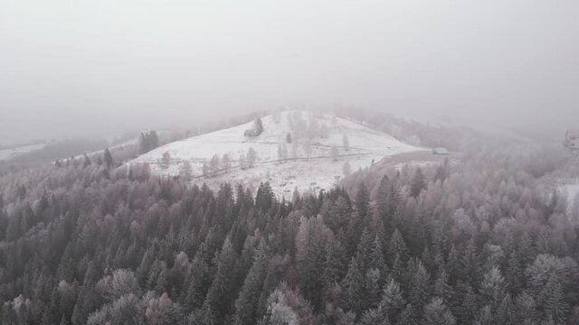 Aerial view of wintertime scene in the Transylvanian village, Pestera, with white frost, fresh snow, blizzard, and fog, at the foot of the Carpathian Mountains