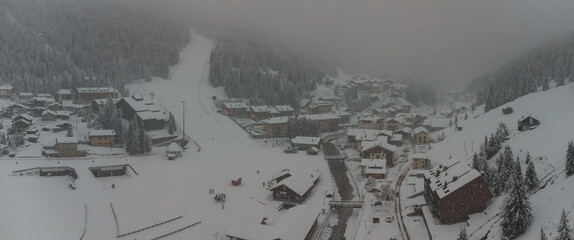 Aerial drone panorama of Santa Caterina di Valfurva village during a heavy snow storm in winter. Visible ski slope and many hotels in the area.