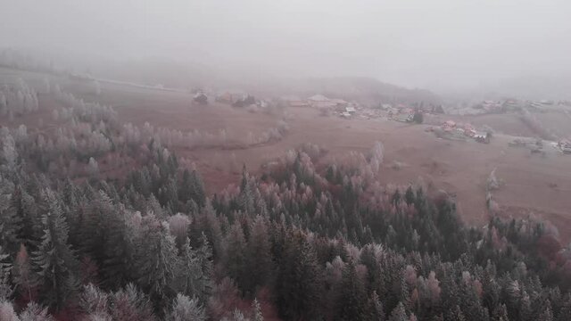 Aerial view of wintertime scene in the Transylvanian village, Pestera, with white frost, fresh snow, blizzard, and fog, at the foot of the Carpathian Mountains