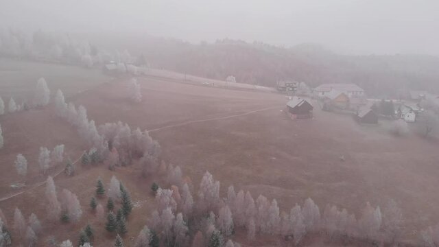 Aerial view of wintertime scene in the Transylvanian village, Pestera, with white frost, fresh snow, blizzard, and fog, at the foot of the Carpathian Mountains