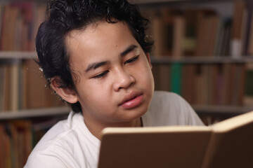 Smart Asian student boy reading a book in library, educational, kid learning at home