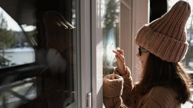 Little girl in a sweater draws a heart in condensation on a balcony window