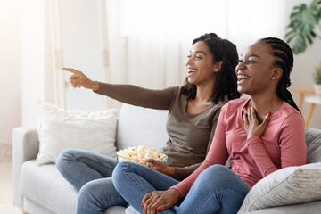 Obraz premium Two black girlfriends having fun at home, watching comedy