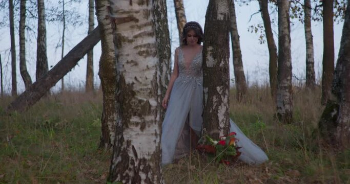 A bride in a gray dress walks with a wedding bouquet in the forest.