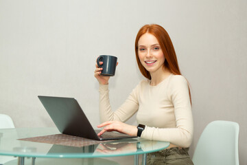 Naklejka premium beautiful young female with red hair at the table with a laptop