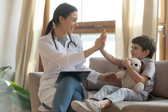 Smiling Young Female Doctor Give High Five To Caucasian Little Boy Patient At Consultation In Clinic. Happy Caring Woman Pediatrician Greet With Small Child At Checkup In Hospital. Healthcare Concept