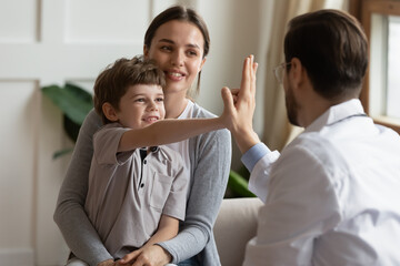 Smiling small boy patient at hospital checkup with mom give high five to male pediatrician or GP....