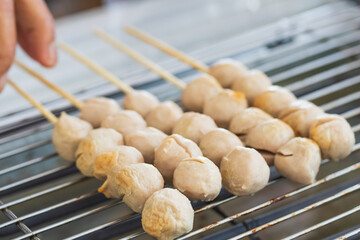 Merchant hands are toasting meatballs that are skewered on charcoal stove with grille. (street food shop)