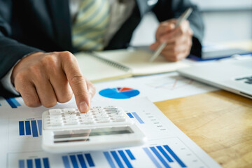 Asian male finance businessmen are calculating Investment results by calculator, Company performance from graph documents On the desk in his office, business ideas for calculating investment results.