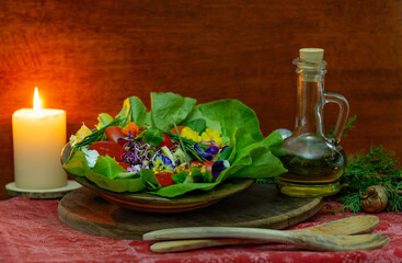 Christmas still life with salad of tomato, cheese, green onions and tricolor violet flowers,  a candle,  wooden spoons, a branch of juniper and a bottle of olive oil