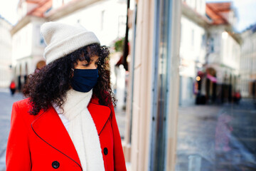 Portrait of a  woman in red shopping outside with face mask  looking at shop window