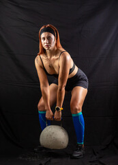Beautiful redhead girl lifts a huge kettlebell in the studio on a black background