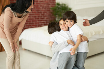 Joyful latin children, teenage girl and two little twin boys hugging each other while having fun indoors. Mom and dad playing with their kids at home