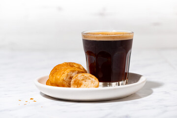 black coffee in a glass and mini croissant