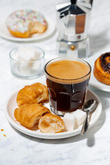 black coffee in a glass, mini croissants and a sweet bun, vertical top view