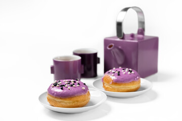 A bun covered with glaze on a white background. Teapot and cups. A set of purple crockery. Still life with cake. Copy space. Card.