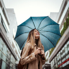 A beautiful smiling young woman walking through the city with an umbrella.