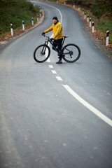 Fototapeta na wymiar Young man taking a brake on a country road during biking through autumn forest