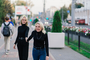 Two young females walking smiling embracing and kissing outdoor in the city