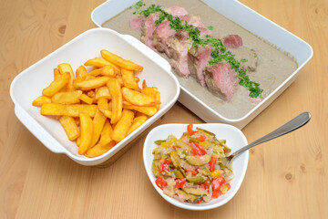 natural fries on a white plate, roasted pork neck with mushroom sauce, salad with zucchini, cucumber and pepper