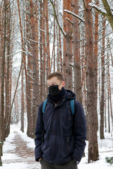 Fototapeta na wymiar A young man wearing a protective mask walks alone in a snowy forest.