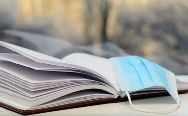 On the open diary are glasses and a medical mask. Light falls from the window. The concept of insulation, the planning of a new day