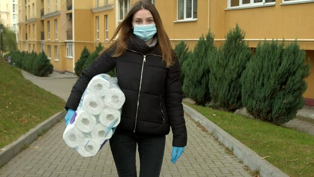 Young blonde girl in a mask walks down the street with toilet paper.4K