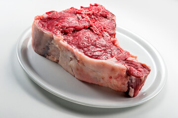 Raw T-bone steak on white round plate
