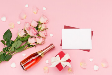 Roses, bottle of wine, empty envelope and gift on pink background. Valentines day concept. Flat lay, top view, copy space.