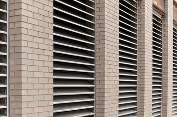 Perspective view of wall of an urban commercial building with numerous inset HVAC air exhaust vents, light colored brick, horizontal aspect