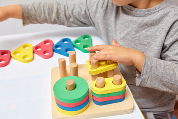 The child collects a sorter. Educational logic toys for kid's. Children's hands close-up. Montessori Games for Child Development. Multicolored logic sorter on white background.