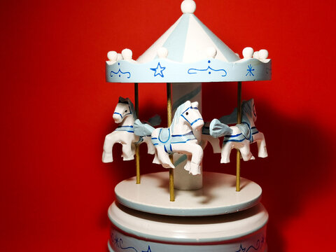 Carousel-shaped music box with wooden horses on red background.