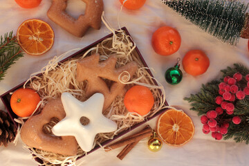 Preparing winter holidays gift box. Flat lay composition with Christmas gingerbread cookies, citrus fruits, ornaments, and Christmas tree on white background.